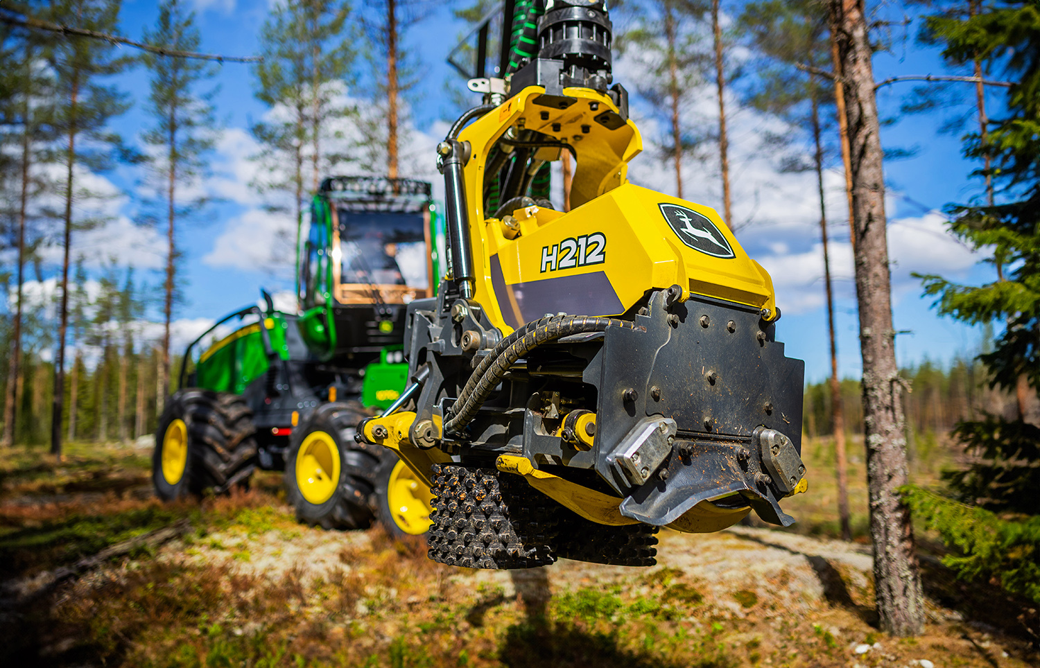 Kuvassa on John Deere harvesteri metsässä, etualalla harvesteripää malliltaan H212.